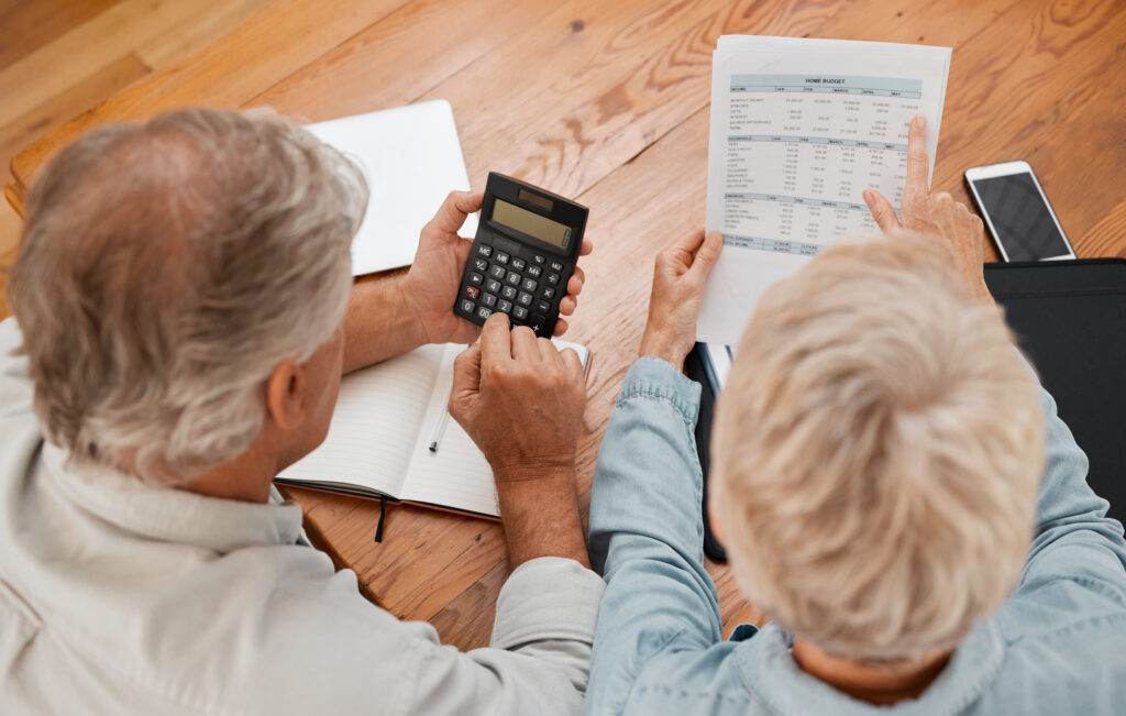 Leisure World Seal Beach - Budget, finance and senior couple with calculator planning financial investments, mortgage and tax papers. Elderly woman counting bills, debt and pension fund on bank statement with partner at home